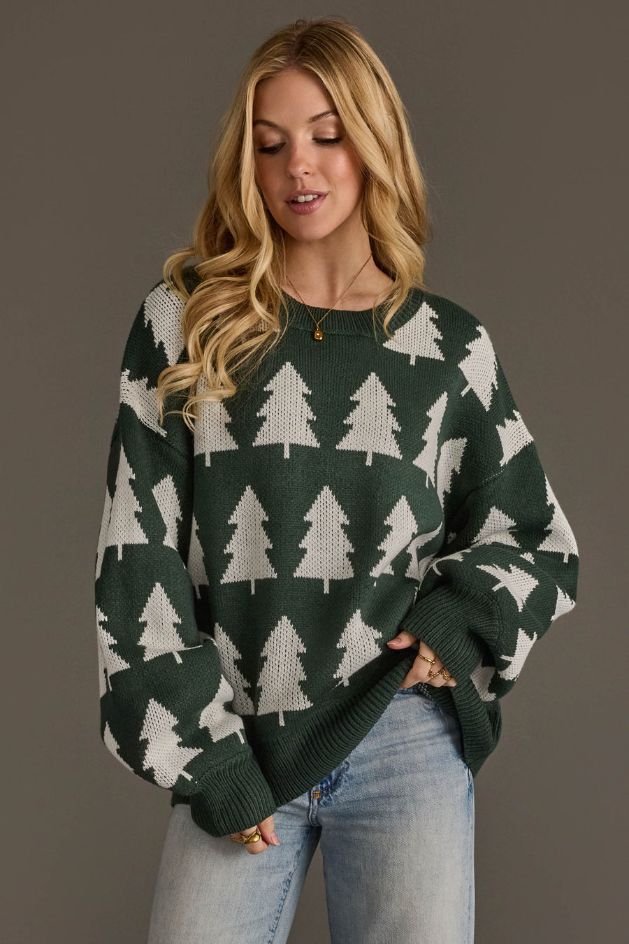 A woman wearing a Green & White Tree Sweater with a white repeating pine tree pattern and light-wash jeans.