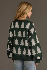 A person wearing a cozy, oversized green and white Green & White Tree Sweater featuring a repeating white pattern of pine trees.
