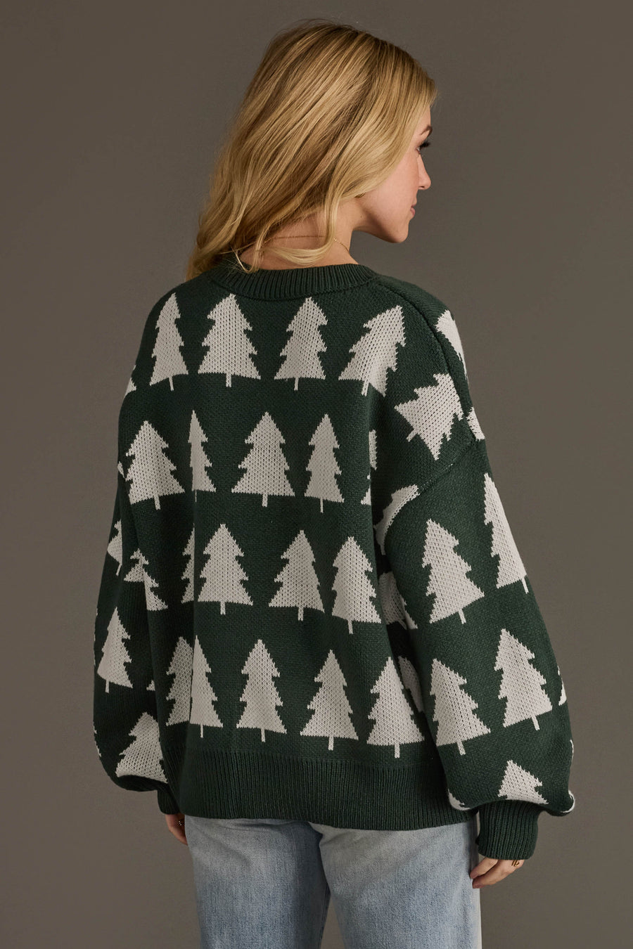 A person wearing a cozy, oversized green and white Green & White Tree Sweater featuring a repeating white pattern of pine trees.