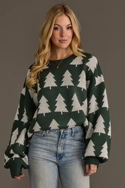 A person wearing a cozy, oversized Green & White Tree Sweater in dark green with a repeating pattern of white pine trees.