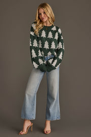 A person wearing a Panache Apparel Collection Green & White Tree Sweater with a white repeating pine tree pattern and light-wash wide-leg jeans.