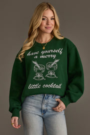 A woman wears a Green Merry Little Cocktail Embroidered Sweatshirt featuring the text have yourself a merry little cocktail and an illustration of two stemmed glasses.
