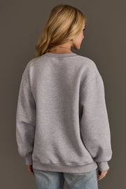 Back view of a person wearing an oversized, plain grey Christmas List Embroidered Sweatshirt.
