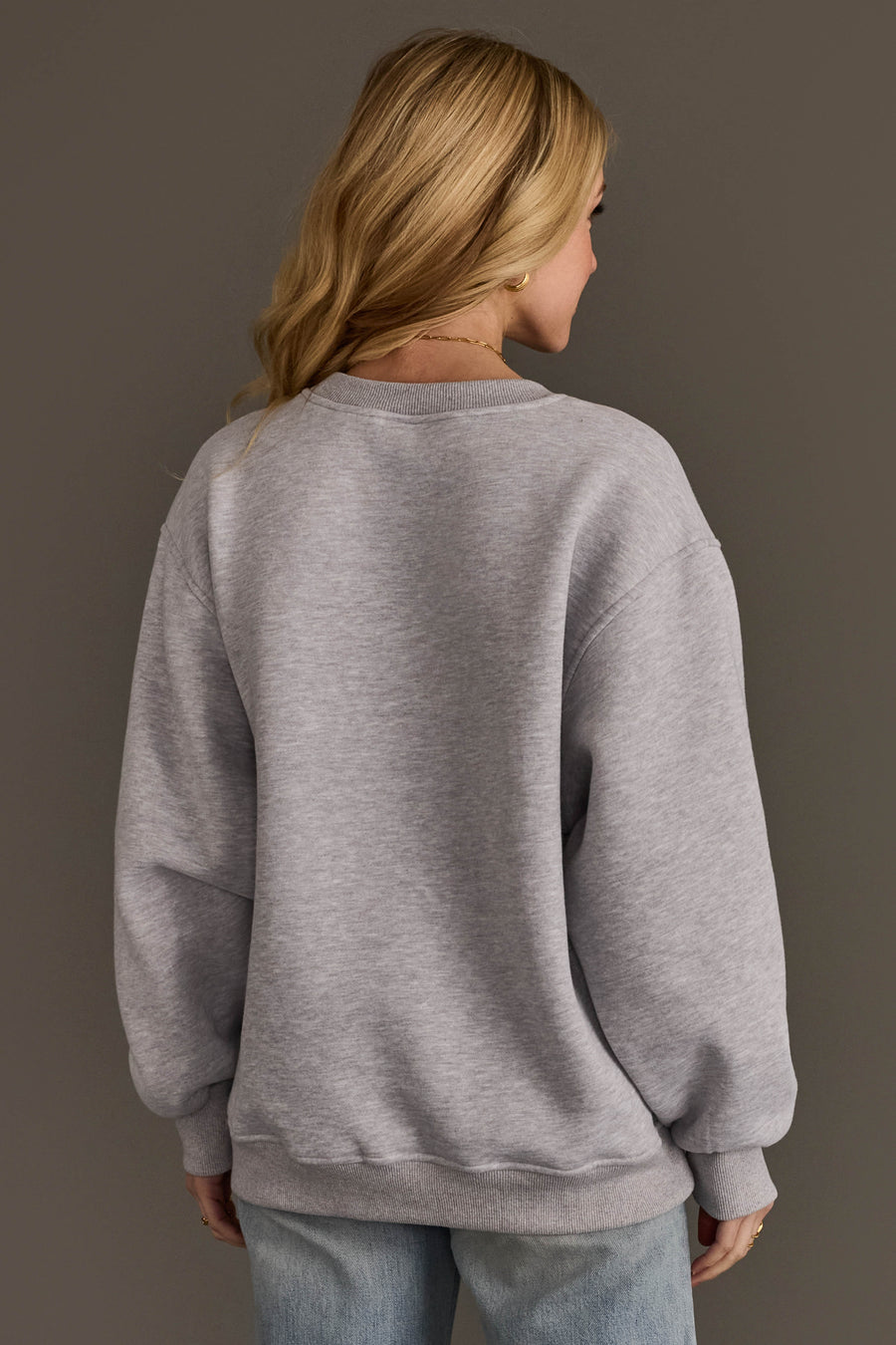 Back view of a person wearing an oversized, plain grey Christmas List Embroidered Sweatshirt.