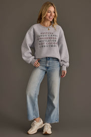 A woman wears a Christmas List Embroidered Sweatshirt featuring a list of embroidered words in red and black, paired with light-wash wide-leg jeans and athletic sneakers.