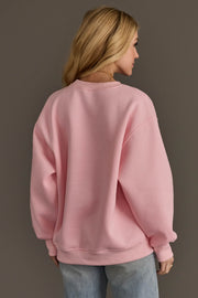 A person wearing a cozy, plain pink Pink Merry Little Cocktail Embroidered Sweatshirt.