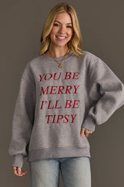 A smiling woman wears a grey You Be Merry Embroidered Sweatshirt by Panache Apparel Collection with the red embroidered text YOU BE MERRY ILL BE TIPSY.