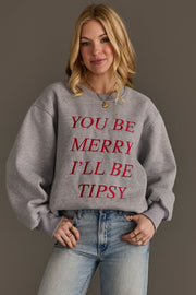 A person wearing the You Be Merry Embroidered Sweatshirt, a cozy, embroidered grey crewneck with the red text YOU BE MERRY ILL BE TIPSY.