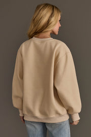 Back view of a person wearing an oversized beige Christmas Graphics Embroidered Sweatshirt and blue jeans.