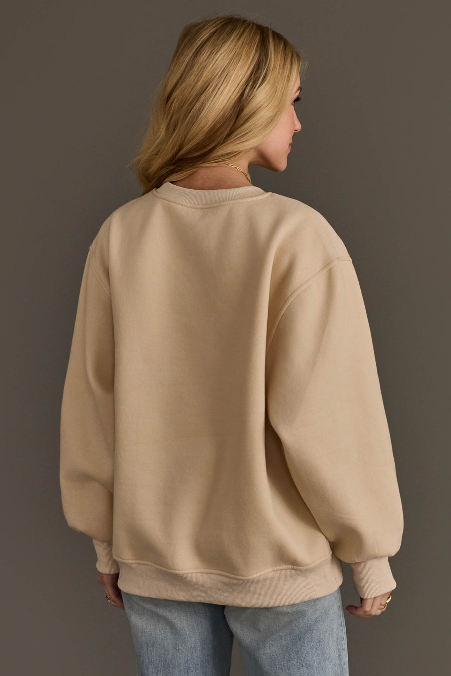 Back view of a person wearing an oversized beige Christmas Graphics Embroidered Sweatshirt and blue jeans.