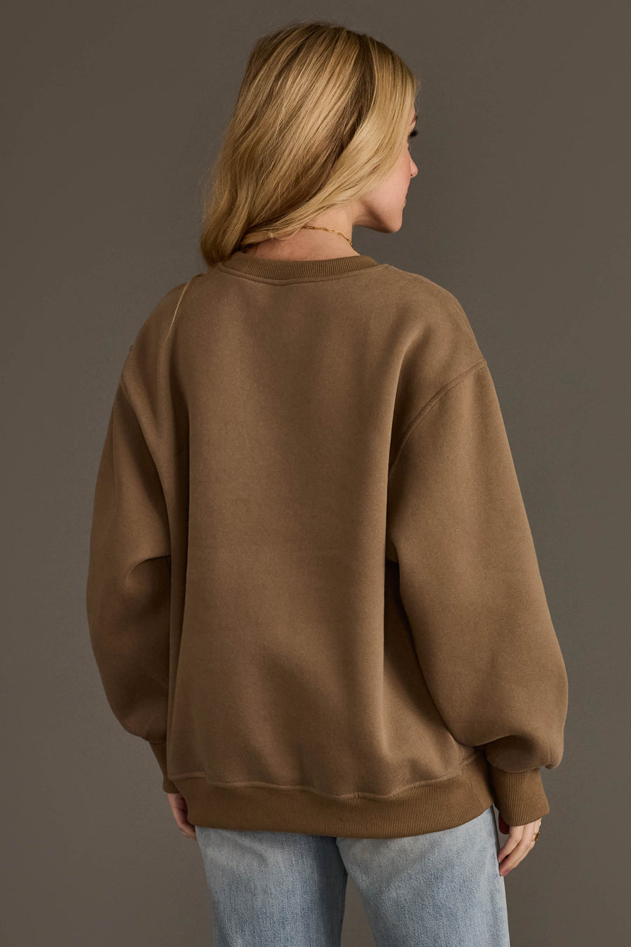 A person with long blonde hair is seen from behind, wearing the Panache Apparel Collection Taupe & Dark Brown Whiskey Weather Sweatshirt and light blue jeans, standing against a neutral background.