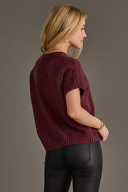 A woman with blonde hair wears the Panache Apparel Collection Maroon Short Sleeve Sweater and black leather pants, standing facing away and looking to the side against a plain gray background.