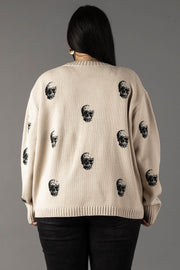 A person with long dark hair, seen from behind, wears the Tan Skull Sweater by panacheaccessories, a relaxed fit tan knit sweater featuring scattered black skull prints, paired with black pants and standing against a plain gray background.