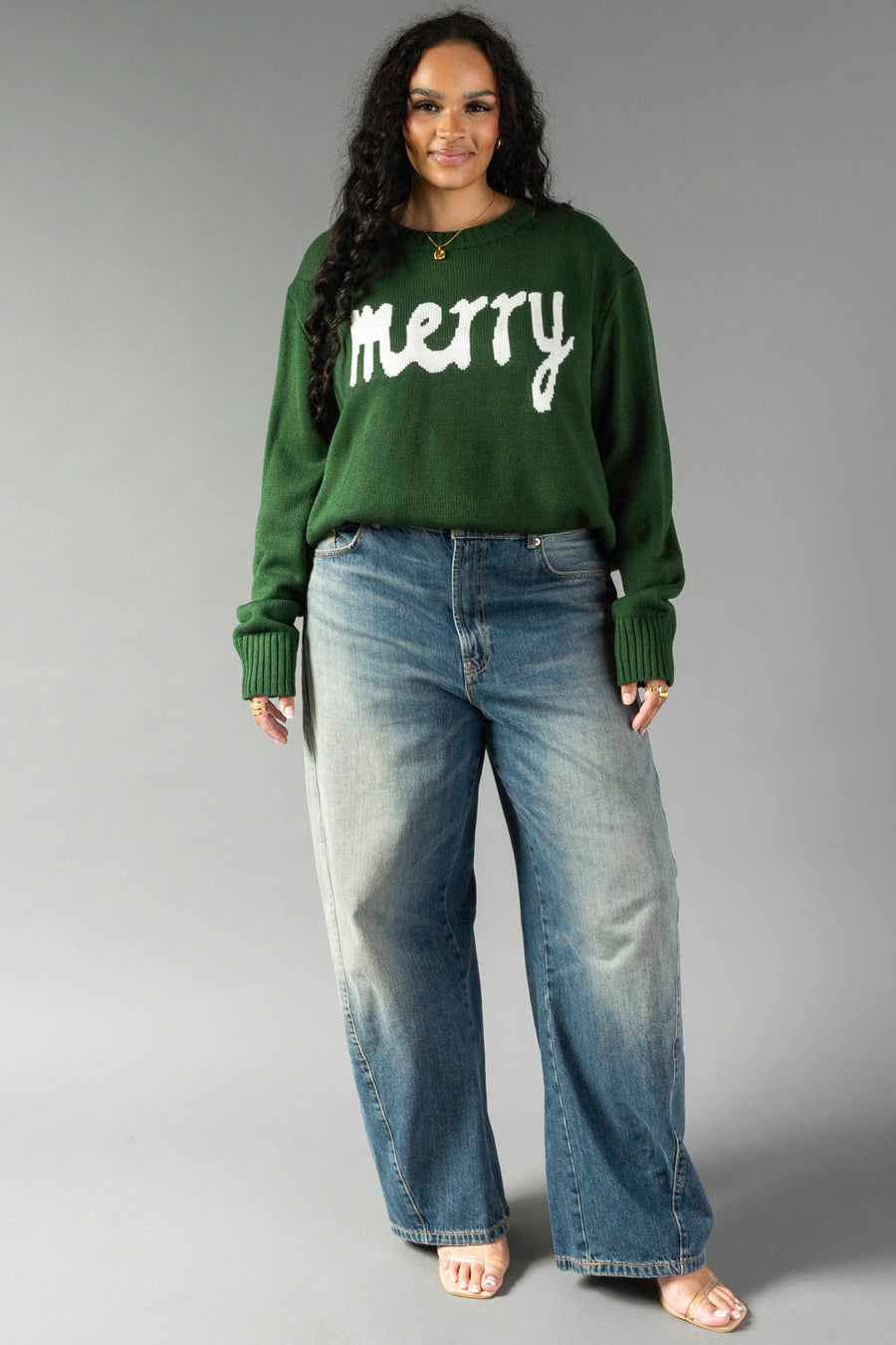 A woman wearing a hunter green Hunter Green Merry Sweater and baggy blue jeans.