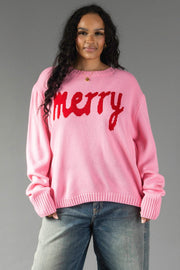 A person wears a relaxed fit pink knit Pink & Red Merry Sweater with the word merry in red script across the chest.