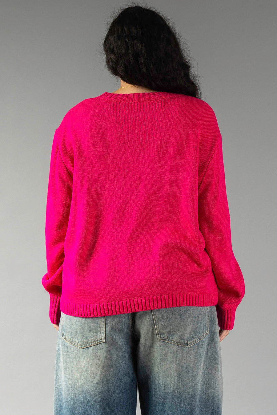 Back view of a person wearing a bright pink Pink & Light Pink Merry Sweater and blue jeans.