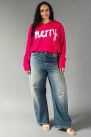 A person wears a bright pink and light pink Merry Sweater with the word written in white script across the chest, paired with wide-leg blue jeans.