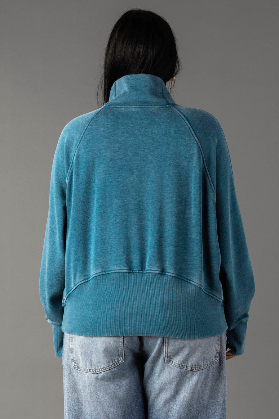 Back view of plus-size woman wearing a dark teal quarter zip sweatshirt.