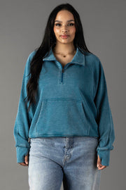 Plus-size woman wearing a dark teal quarter zip sweatshirt with an open collar.