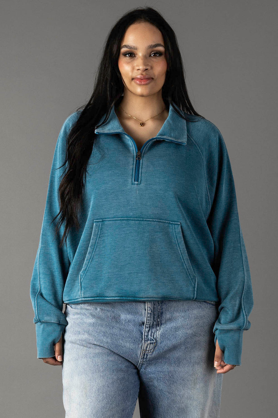 Plus-size woman wearing a dark teal quarter zip sweatshirt with an open collar.