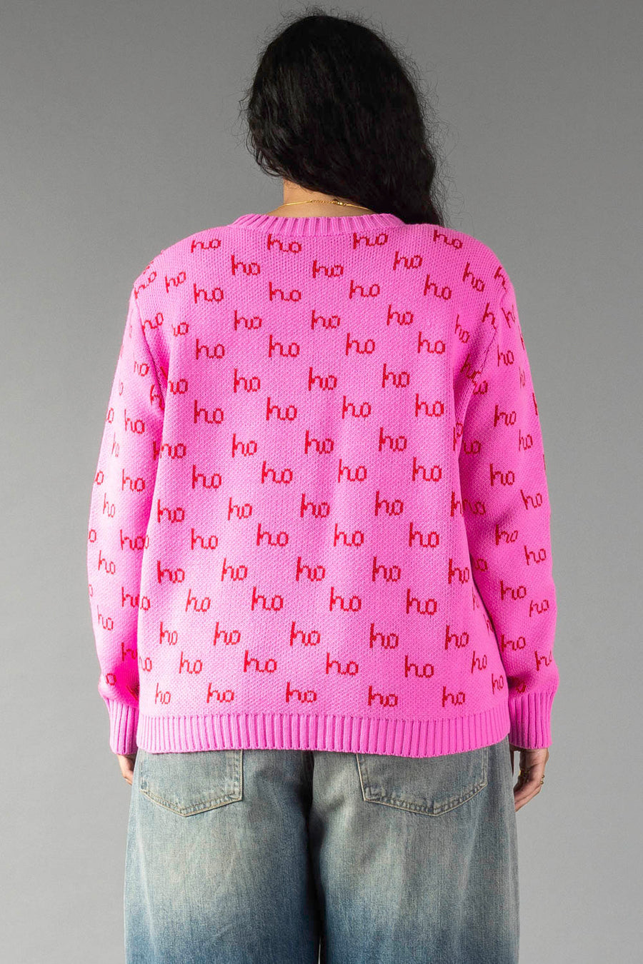 A person seen from behind wears a relaxed fit, pink crewneck Pink Ho Ho Ho Sweater patterned with the repeated word ho in red.