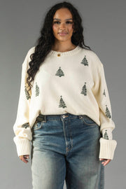 Ivory Festive Tree Sweater in a relaxed knit with small green Christmas trees, worn with blue jeans.