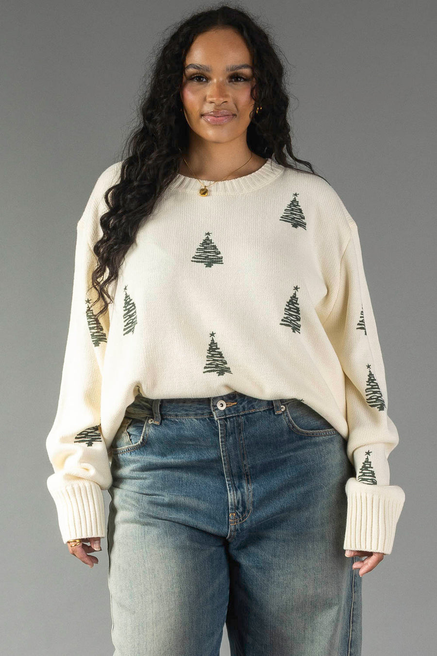 Ivory Festive Tree Sweater in a relaxed knit with small green Christmas trees, worn with blue jeans.