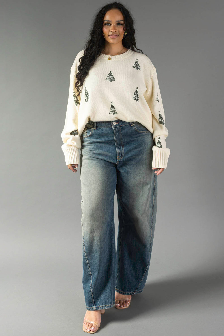 A person wears an Ivory Festive Tree Sweater paired with wide-leg blue jeans.