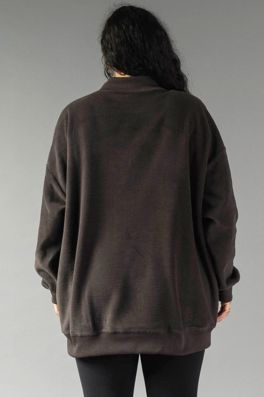 A person with long dark hair, seen from behind, wears the Panache Apparel Collection Dark Gray Game Day & Sunday Funday Reversible Sweatshirt and black pants against a plain gray background.