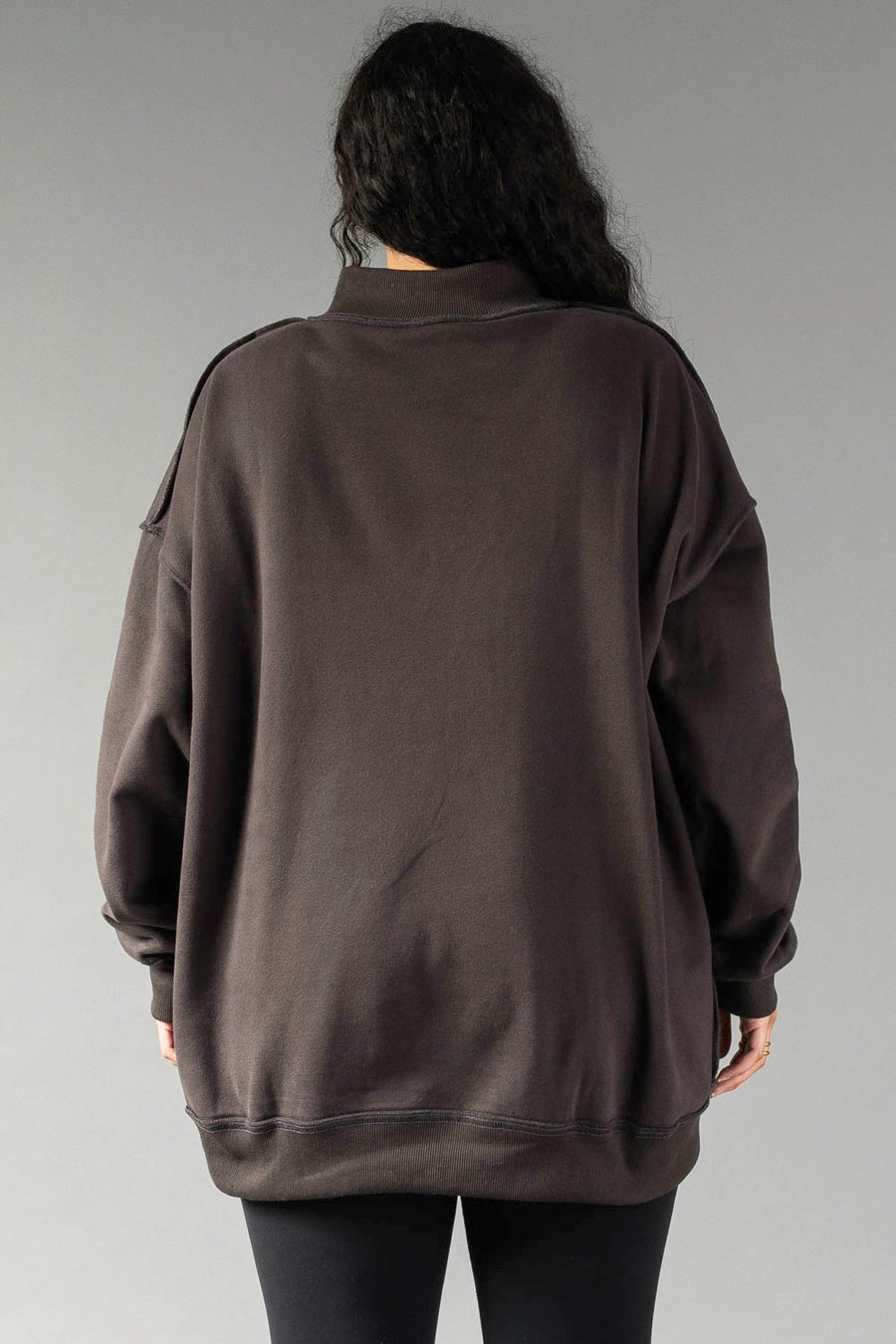 A person with long dark hair wears a Dark Gray Game Day & Sunday Funday Reversible Sweatshirt by Panache Apparel Collection and black pants, standing with their back to the camera against a neutral gray background.