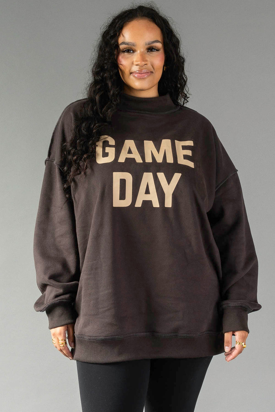 A woman with long curly hair wears the Panache Apparel Collection Dark Gray Game Day & Sunday Funday Reversible Sweatshirt and black leggings, standing against a plain gray background.