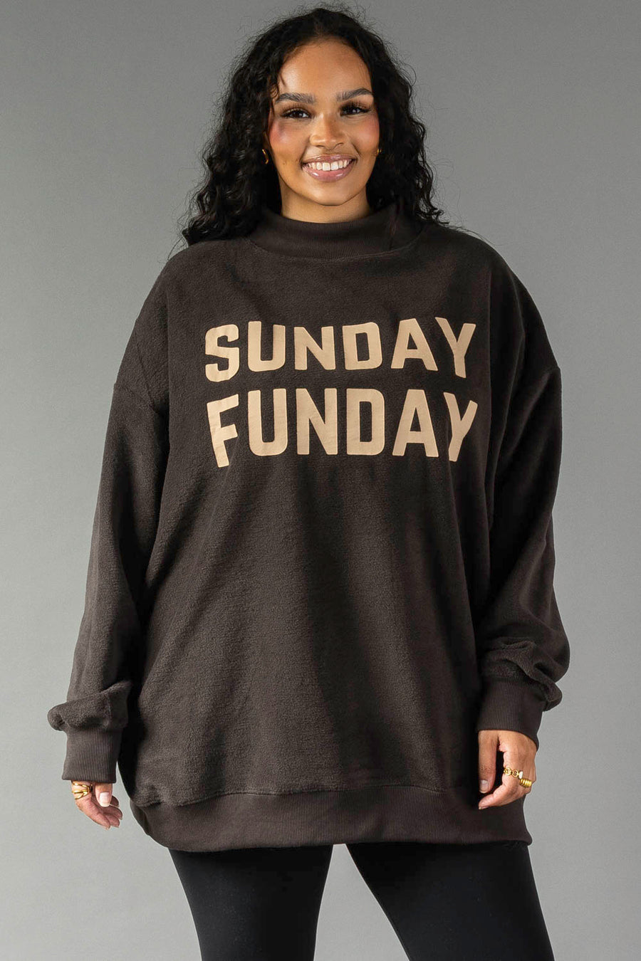 A woman smiles while wearing the Panache Apparel Collection Dark Gray Game Day & Sunday Funday Reversible Sweatshirt, featuring bold beige lettering, against a plain gray background.