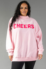 A person wears a light pink Pink Merry & Cheers Reversible Sweatshirt with the word CHEERS printed in bold magenta letters across the chest.