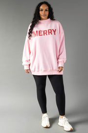A person wearing a Pink Merry & Cheers Reversible Sweatshirt, featuring an oversized light pink fit with red MERRY lettering, paired with black leggings and white sneakers.