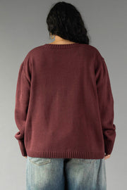 A person with long dark hair is shown from behind, wearing the Panache Apparel Collection Burgundy & Light Pink Wine Season Sweater paired with blue jeans, standing against a plain gray backdrop.