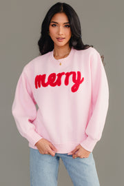 A woman wears a cozy Light Pink & Red Merry Sweatshirt featuring the word merry in red textured lettering across the chest.