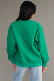 A person seen from behind wearing a cozy Green & White Merry Sweatshirt in green and light blue jeans.