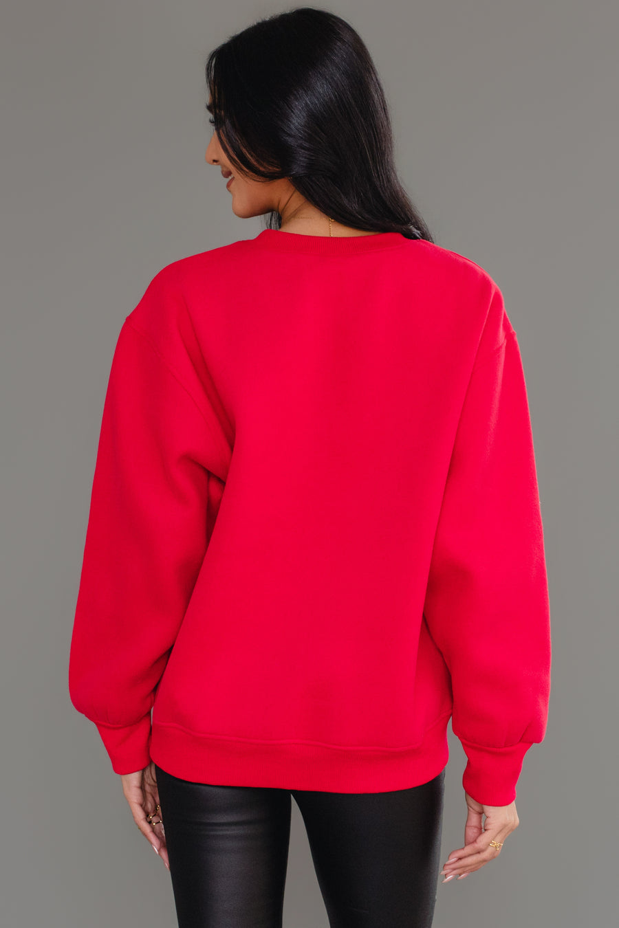 A person viewed from the back wearing a cozy, bright red Red & White Merry Sweatshirt and black pants.