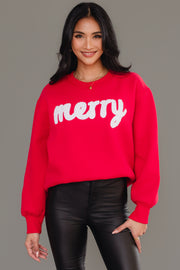 A woman wearing a cozy Red & White Merry Sweatshirt in red with the word merry in white fuzzy script lettering.