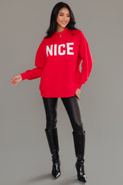 A woman wearing a red Panache Apparel Collection Red Nice & Naughty Reversible Sweatshirt with the word NICE printed in white, black pants, and knee-high boots.
