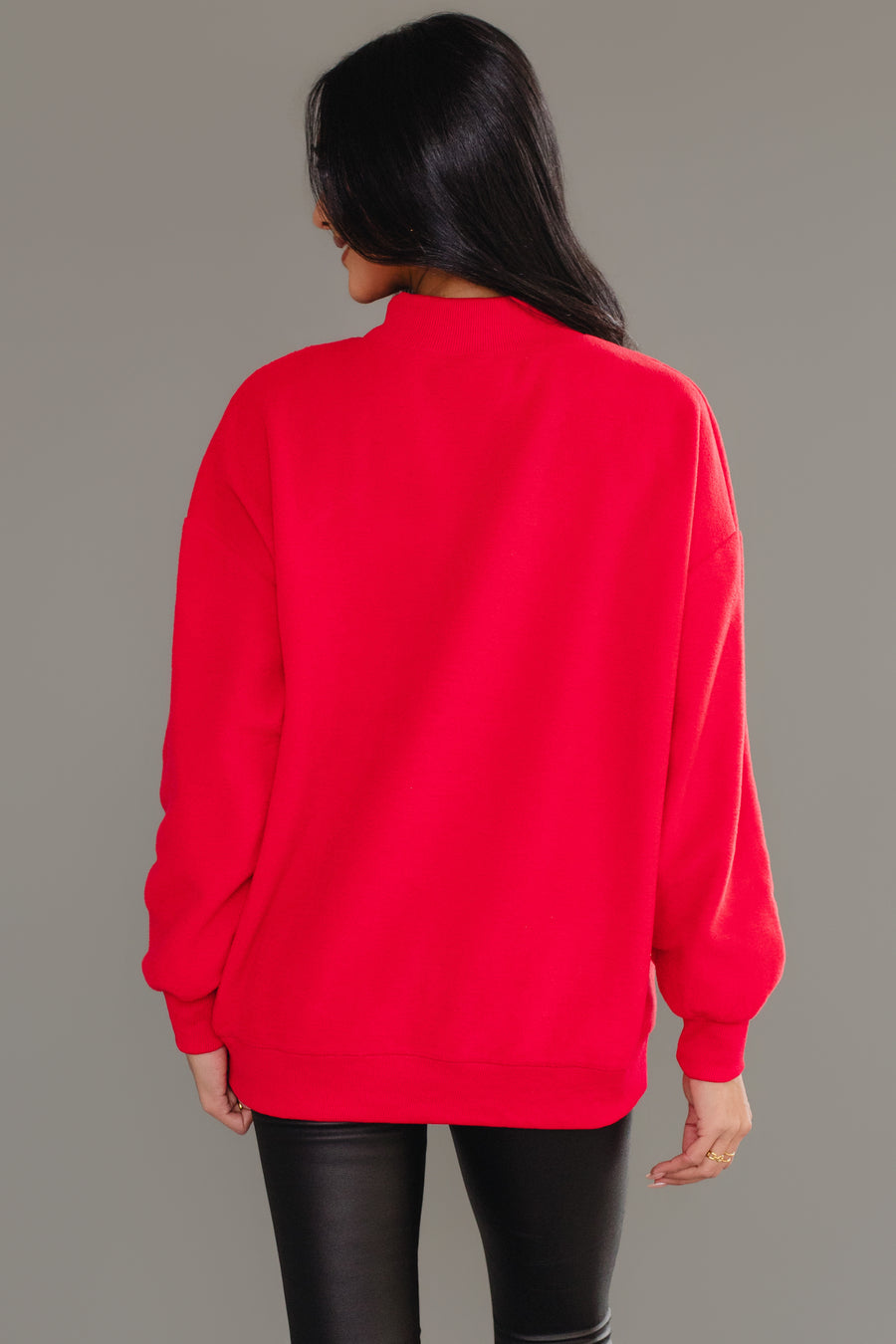 A person seen from behind wears a red Red Nice & Naughty Reversible Sweatshirt with a mock neck and black pants, styled as a cozy holiday outfit.