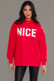 A person wears a cozy, bright red Red Nice & Naughty Reversible Sweatshirt with the word NICE printed in large white capital letters across the chest.
