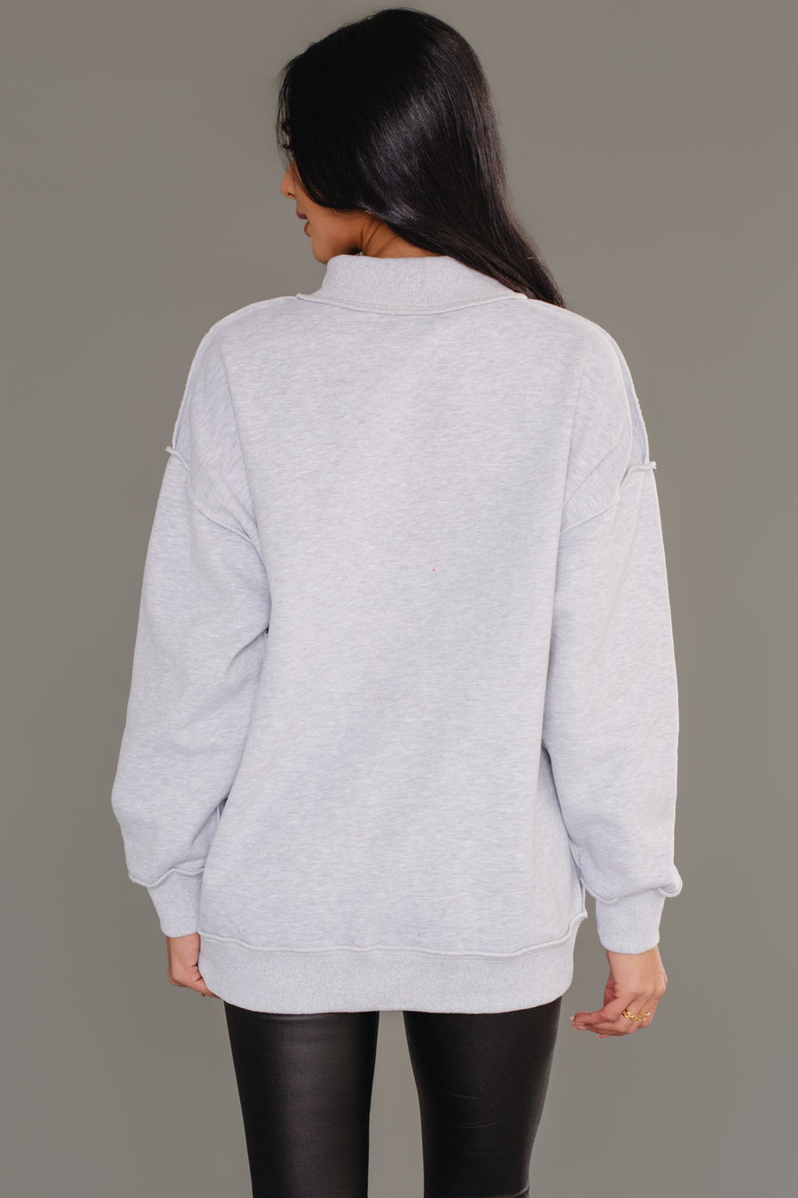 A person seen from the back wearing a cozy, long-sleeved gray Nice & Naughty Reversible Sweatshirt with a mock neckline and black leggings.