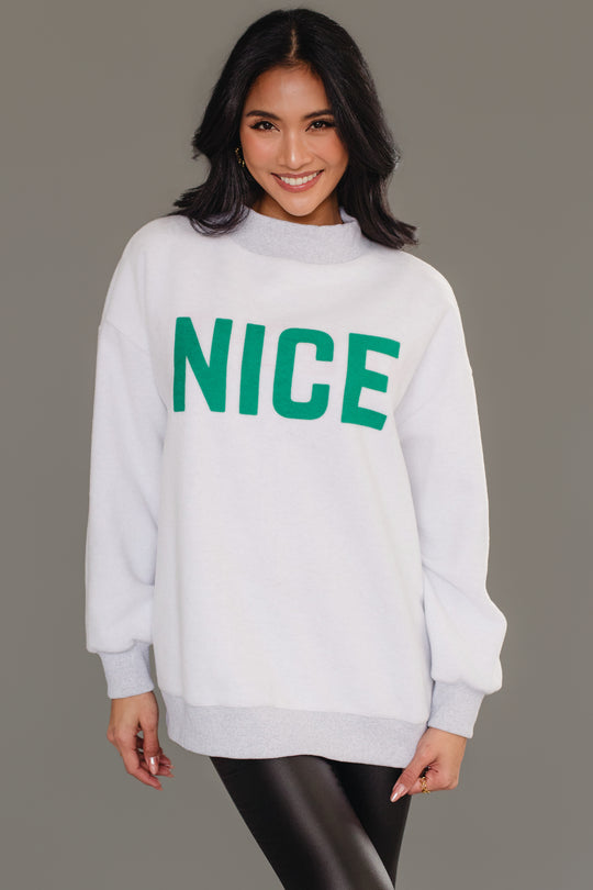 A person wearing a cozy, light gray, reversible Gray Nice & Naughty Reversible Sweatshirt from Panache Apparel Collection with the word NICE in green lettering on the chest.
