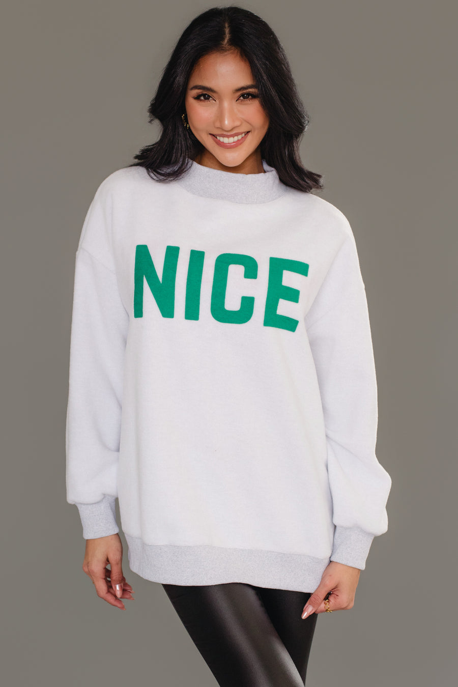 A person wearing a cozy, light gray, reversible Gray Nice & Naughty Reversible Sweatshirt from Panache Apparel Collection with the word NICE in green lettering on the chest.