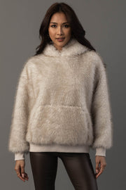 A woman stands against a gray background, facing forward with her hands relaxed by her sides, wearing the Panache Apparel Collection Cream Faux Fur Hooded Sweatshirt and dark pants.