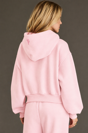 A person with blonde hair wears the Light Pink Panache Cropped Hooded Sweatshirt from Panache Apparel Collection, paired with matching sweatpants, facing away from the camera against a plain, dark background.