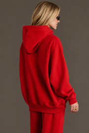 A person with blonde hair, wearing black sunglasses and the hood up on a Panache Apparel Collection Red Panache Hooded Sweatshirt, along with matching red pants, stands facing sideways against a plain background.