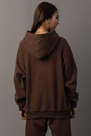 A person with long brown hair is seen from behind, wearing the Brown Panache Hooded Sweatshirt and matching pants from the Panache Apparel Collection, set against a gray background.