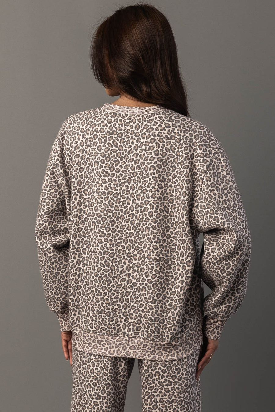 A person with long brown hair is seen from behind against a plain gray background, wearing the Panache Apparel Collection Cream & Brown Leopard Sweatshirt.